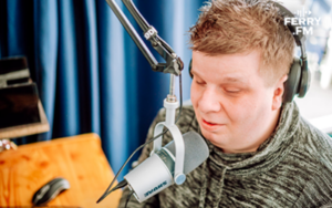 Ferry spreekt in een microfoon met een koptelefoon op in een opnamestudio.